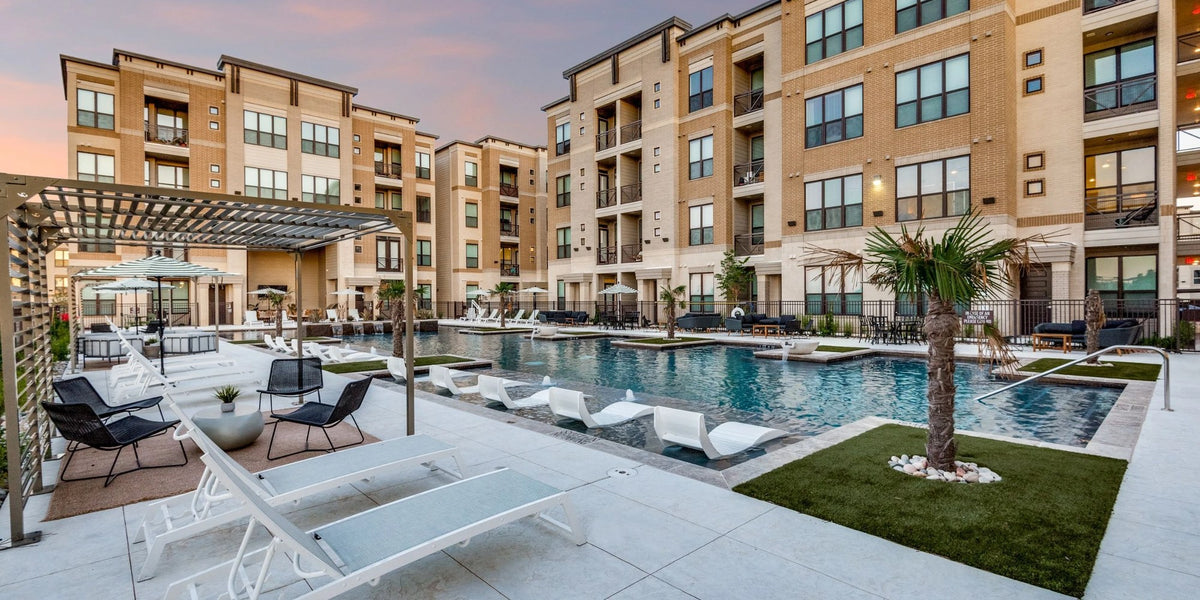 Apartment community courtyard and resort-style pool lit at dusk, with warm exterior and balcony lighting across the buildings